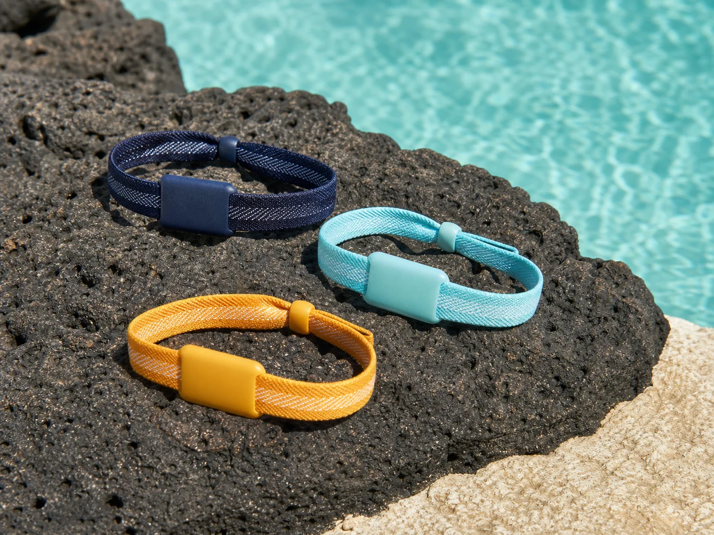Three unbranded woven RFID wristbands on volcanic stone beside a pool